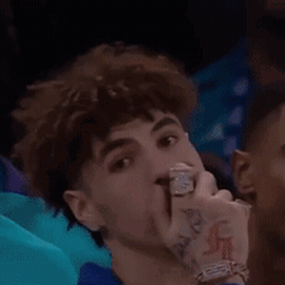A Young Man With A Tattoo On His Wrist Is Sitting In A Crowd Watching A Game . GIF