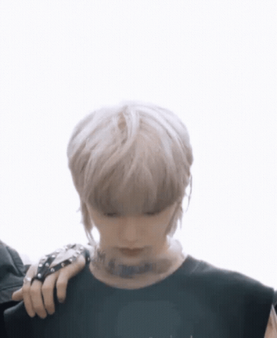 A Young Man With Blonde Hair And A Tattoo On His Neck Is Wearing A Black Shirt And A Black Glove . GIF