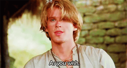 A Young Man With Blonde Hair And Blue Eyes Is Standing In Front Of A Stone Wall . GIF