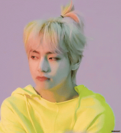 A Young Man With Blonde Hair In A Ponytail Is Wearing A Bright Yellow Hoodie . GIF