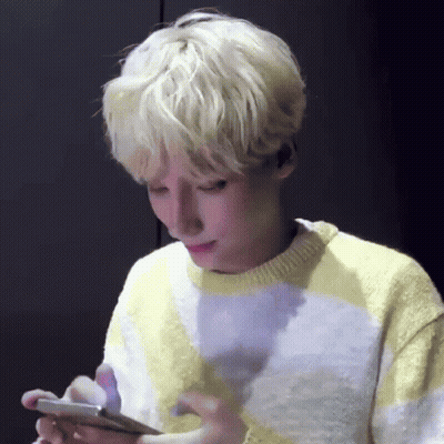 A Young Man With Blonde Hair Is Looking At His Cell Phone . GIF