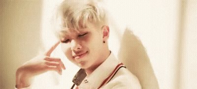 A Young Man With Blonde Hair Is Sitting In Front Of A Window With His Hand On His Head . GIF