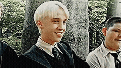 A Young Man With Blonde Hair Is Smiling While Standing Next To A Group Of Young Men . GIF