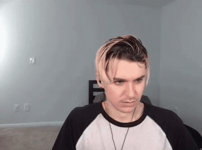 A Young Man With Blonde Hair Is Wearing A Black And White Shirt And A Necklace . GIF