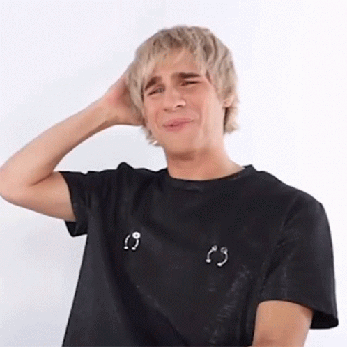 A Young Man With Blonde Hair Is Wearing A Black T-Shirt With Piercings On The Breasts . GIF