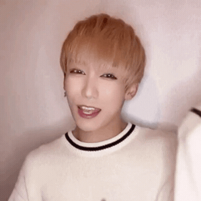 A Young Man With Blonde Hair Is Wearing A White Sweater With A Black Stripe Around The Neck . GIF