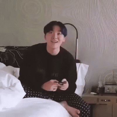 A Young Man With Blue Hair Is Sitting On A Bed Playing A Video Game GIF