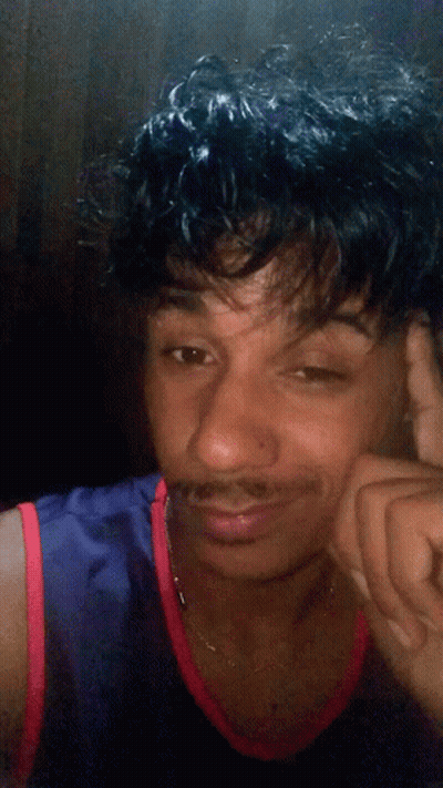 A Young Man With Curly Hair And A Mustache Is Wearing A Blue And Red Tank Top GIF