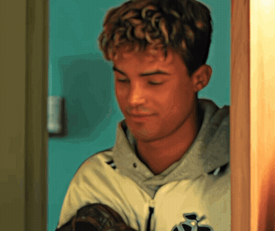 A Young Man With Curly Hair Is Holding A Baseball Glove And Wearing A Jacket With The Letter S On It GIF