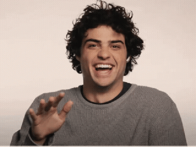 A Young Man With Curly Hair Is Laughing And Waving His Hand GIF