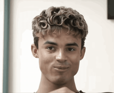 A Young Man With Curly Hair Is Making A Face GIF