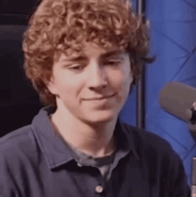 A Young Man With Curly Hair Is Sitting In Front Of A Microphone . GIF