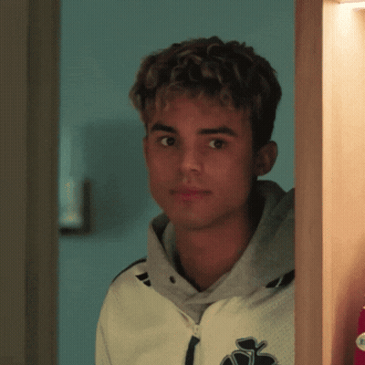A Young Man With Curly Hair Is Standing In A Room GIF