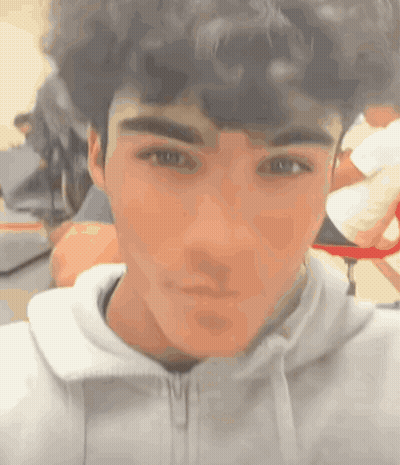 A Young Man With Curly Hair Is Taking A Selfie In A Classroom . GIF