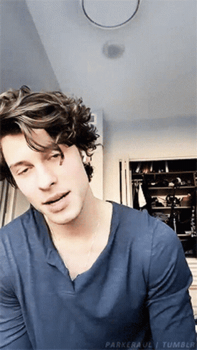 A Young Man With Curly Hair Is Wearing A Blue Shirt And Looking At The Camera . GIF