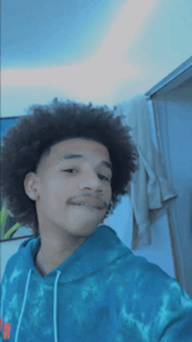 A Young Man With Curly Hair Is Wearing A Blue Tie Dye Sweatshirt GIF