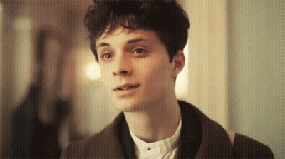 A Young Man With Curly Hair Is Wearing A Brown Jacket And A White Shirt GIF