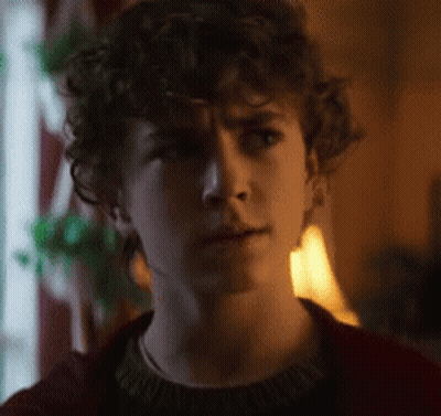 A Young Man With Curly Hair Is Wearing A Red Sweater . GIF