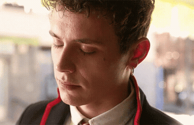 A Young Man With Curly Hair Is Wearing A Suit And Tie With His Eyes Closed GIF