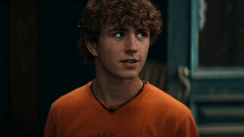 A Young Man With Curly Hair Is Wearing An Orange Shirt That Says Abercrombie GIF