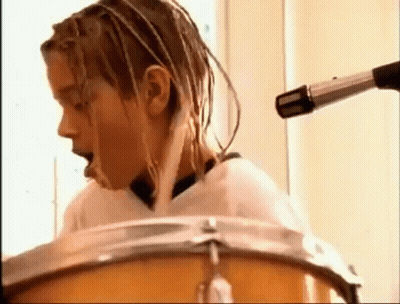 A Young Man With Dreadlocks Is Playing Drums In Front Of A Microphone . GIF