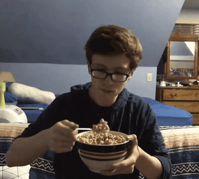 A Young Man With Glasses Is Eating Cereal From A Bowl GIF