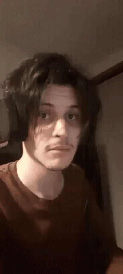 A Young Man With Long Black Hair And Headphones Is Making A Funny Face . GIF