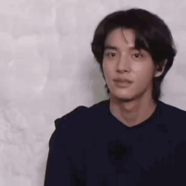 A Young Man With Long Black Hair Is Wearing A Black Shirt And Looking At The Camera . GIF
