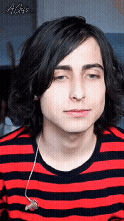 a young man with long black hair is wearing a red and black striped shirt and ear buds .