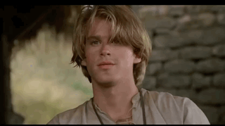 A Young Man With Long Blonde Hair Is Standing In Front Of A Brick Wall . GIF