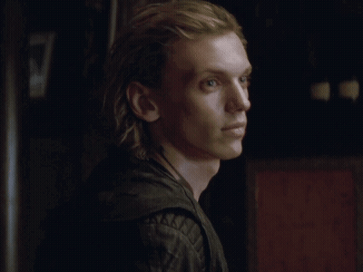 A Young Man With Long Blonde Hair Is Wearing A Black Leather Jacket And A Necklace . GIF