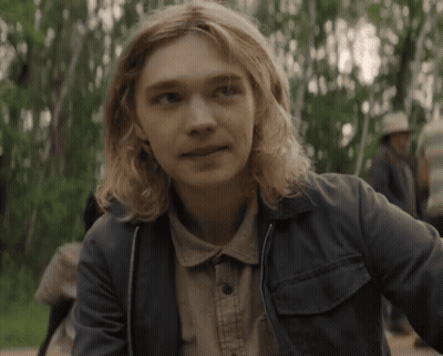 A Young Man With Long Blonde Hair Is Wearing A Denim Jacket GIF