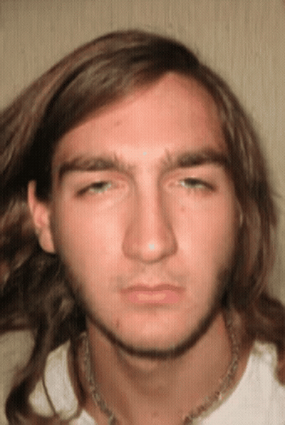 A Young Man With Long Hair And A Necklace Around His Neck Looks At The Camera GIF