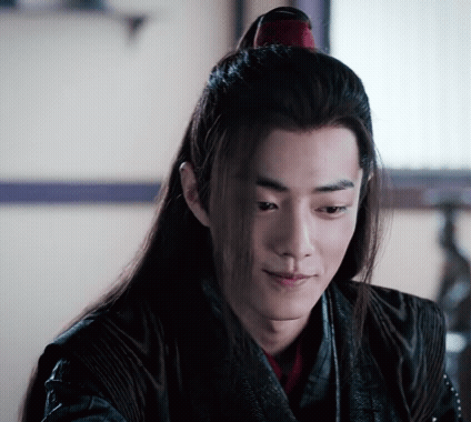 A Young Man With Long Hair And A Ponytail Is Sitting In Front Of A Window . GIF