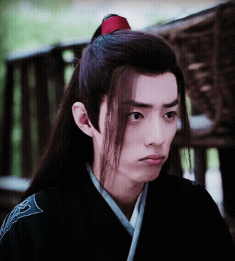 A Young Man With Long Hair And A Red Ponytail Looks At The Camera GIF