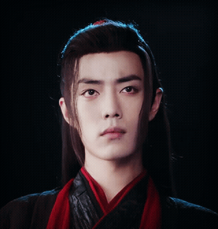 A Young Man With Long Hair And A Red Scarf Around His Neck Looks At The Camera GIF