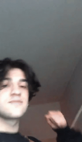 A Young Man With Long Hair Is Making A Funny Face While Standing In A Room . GIF