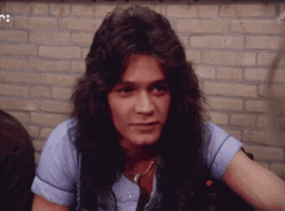 A Young Man With Long Hair Is Sitting In Front Of A Brick Wall And Looking At The Camera . GIF