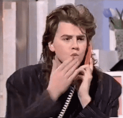 A Young Man With Long Hair Is Talking On A Telephone . GIF