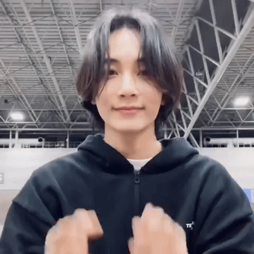 A Young Man With Long Hair Is Wearing A Black Hoodie And Making A Peace Sign . GIF