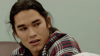 A Young Man With Long Hair Wearing A Plaid Shirt Looks At The Camera GIF