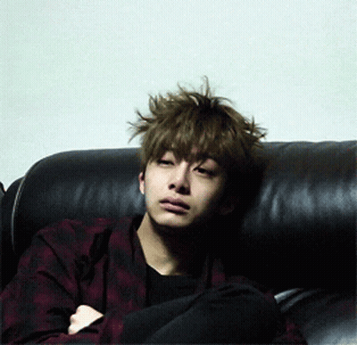 A Young Man With Messy Hair Is Sitting On A Black Couch GIF