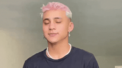 A Young Man With Pink Hair And Pearl Necklace Is Wearing A Black Shirt And Earrings . GIF