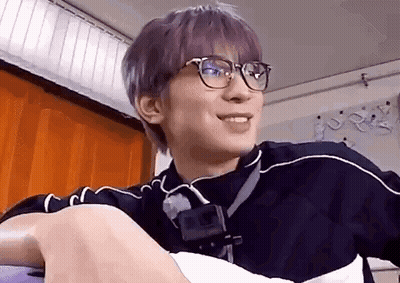 A Young Man With Purple Hair And Glasses Is Sitting On A Couch . GIF