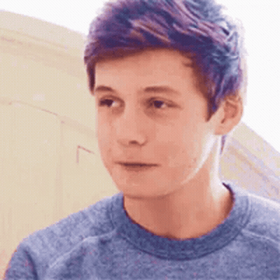 A Young Man With Purple Hair Is Wearing A Blue Shirt And Looking At The Camera . GIF