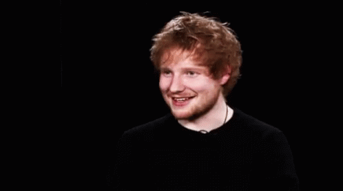 A Young Man With Red Hair And A Beard Is Smiling In A Black Shirt . GIF