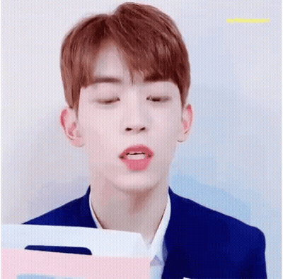 A Young Man With Red Hair Is Smiling While Holding A Pink And Blue Folder . GIF