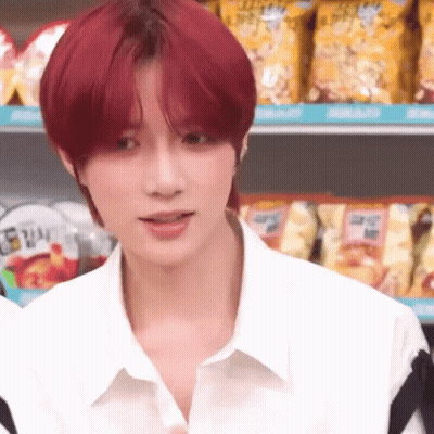 A Young Man With Red Hair Is Wearing A White Shirt And Standing In Front Of A Shelf Of Chips . GIF