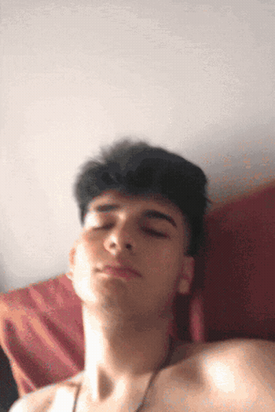 A Young Man Without A Shirt Is Laying On A Bed With His Eyes Closed GIF