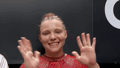 A Young Woman In A Red Dress Is Smiling And Waving Her Hands . GIF